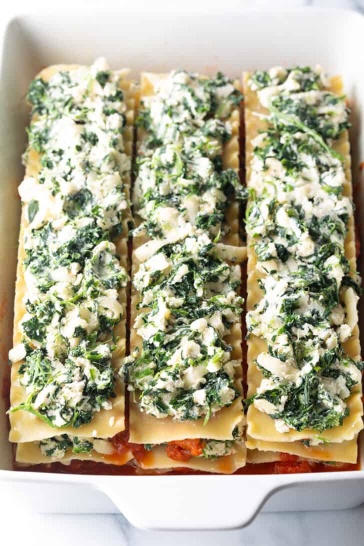 Layers in a large white rectangle baking dish, the layer shows creamy spinach and cheese spread across noodles.