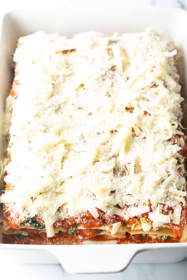 Layers in a large white rectangle baking dish, shredded parmesan and mozzarella cheese are the top layer.