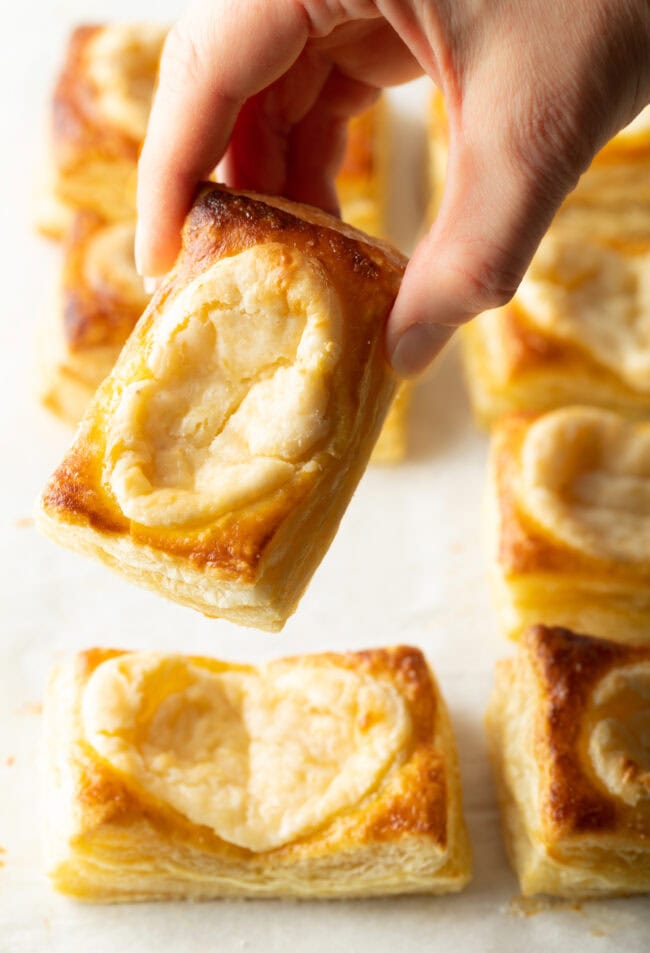 Hand holding a baked danish with cream cheese center to camera.