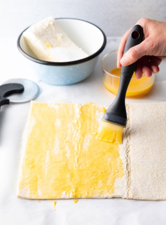 Hand with pastry brush, brushing egg wash on puff pastry.