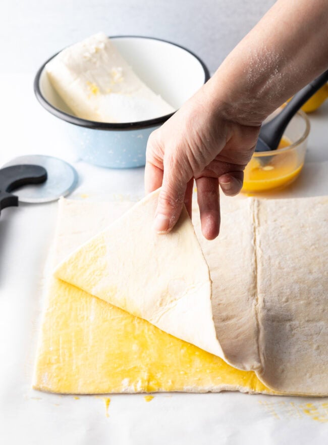 Hand adding a layer of puff pastry on top of layer brushed with egg.