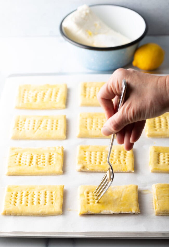 Hand with fork poking whole in rectangles of puff pastry.