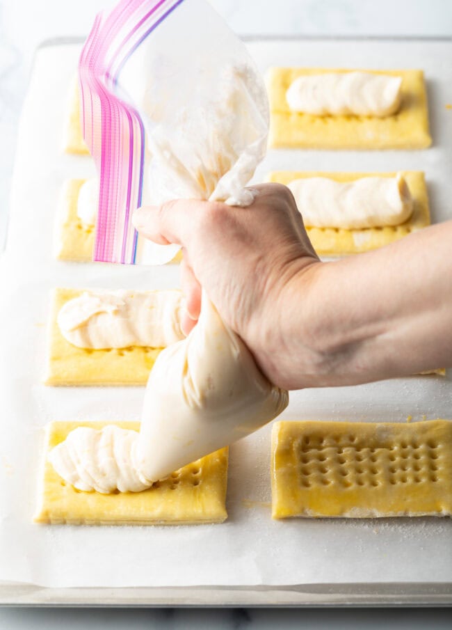 Hand with piping bag adding filling mixture to the danishes.