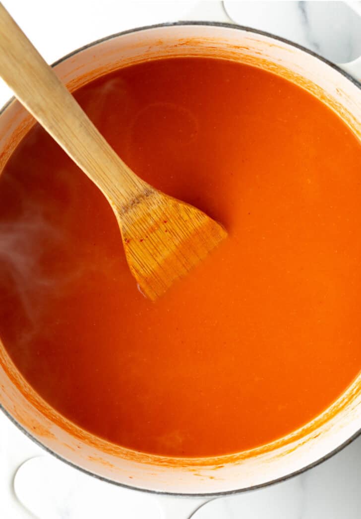 Top down view creamy tomato soup in a large pot with a wood spatula.