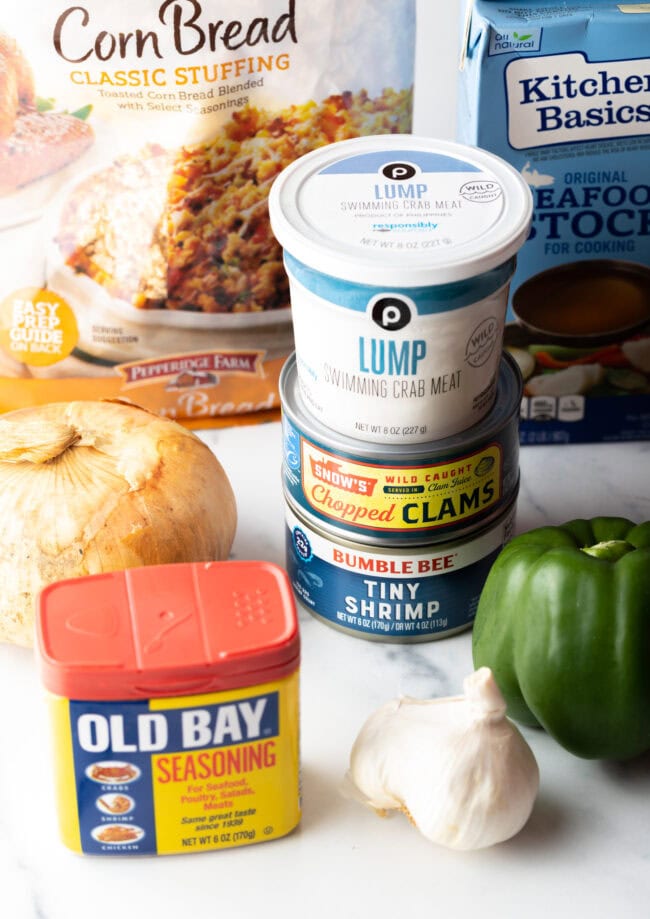 Recipe ingredients: Containers of clams, cornbread stuffing, bell pepper, garlic, onion, lump crab meat, and jar of old bay seasoning.