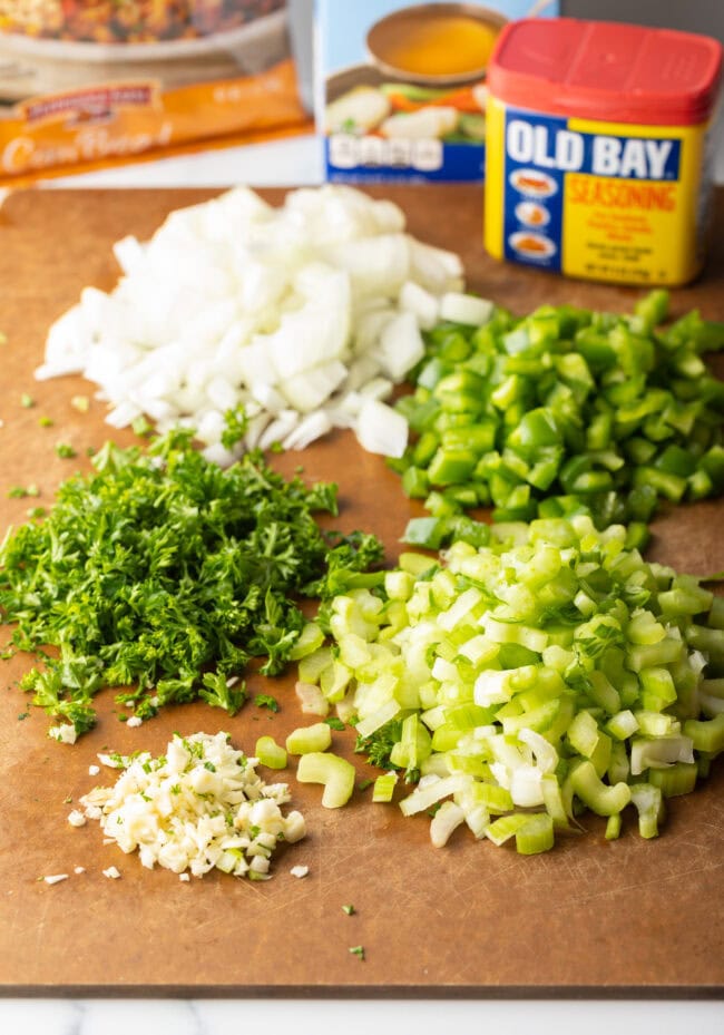 Chopped piles of ingredients on a cutting board: Onion, green pepper, garlic, celery, and parsley.