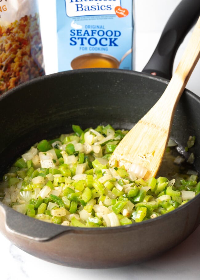 Sauteeing green veggies and aromatics in a black skillet with wooden spatula.