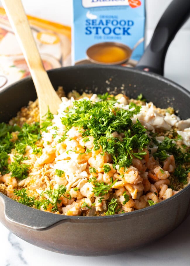 Onion, green pepper, garlic, celery, and parsley stirred into the seafood cooking in a heavy black skillet.