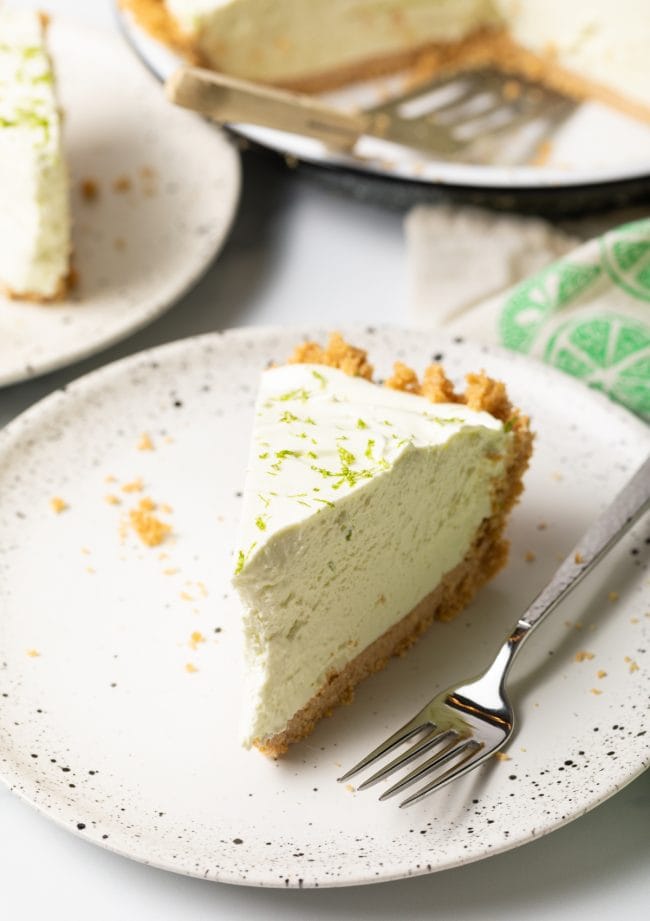 Slice of no-bake key lime pie on a white plate with a fork. 