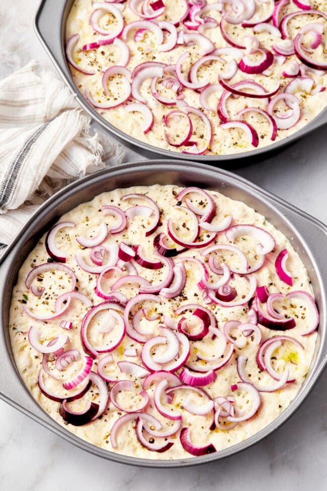 How to Make Focaccia Bread - dough in a cake pan with onions on top.