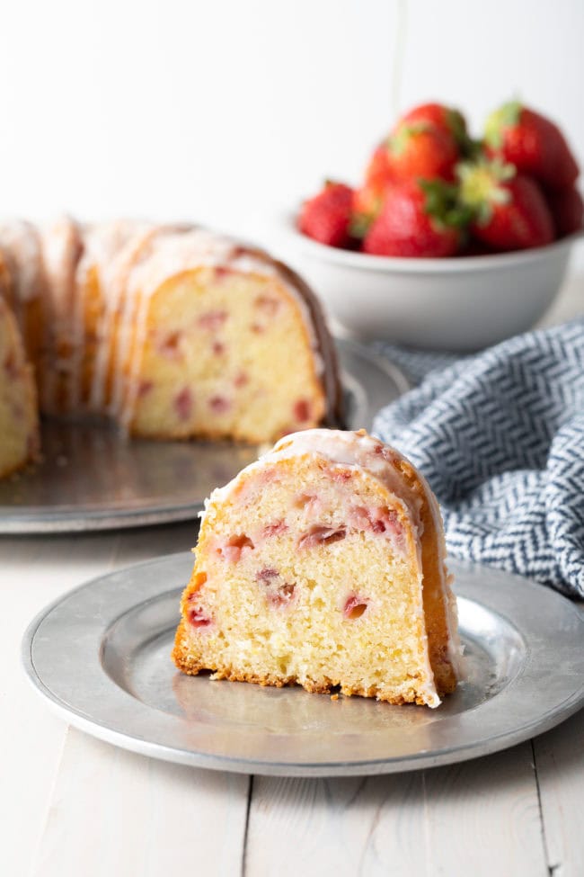 Slice of bundt cake recipe on a plate with the rest of the cake in the background. 