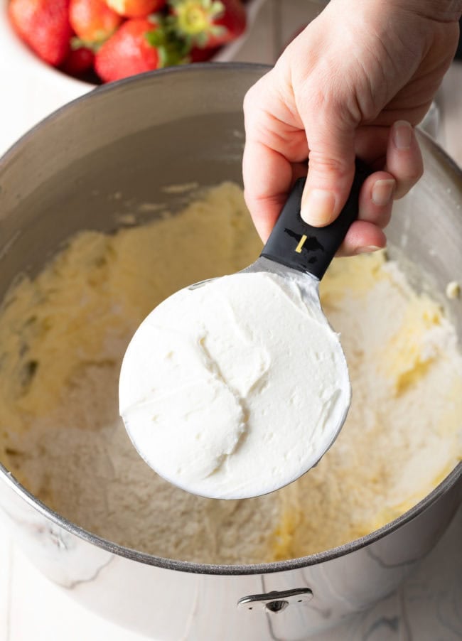 Strawberry Cake Batter with hand holding a measuring cup with yogurt in it. 