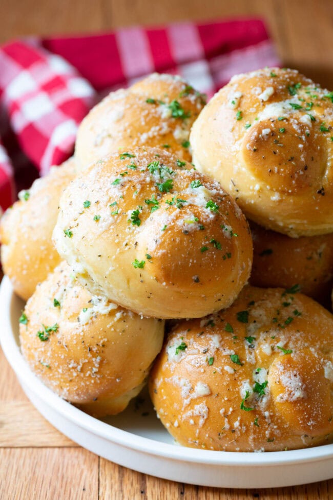 Garlic knots piled on top of each other on a white plate. 