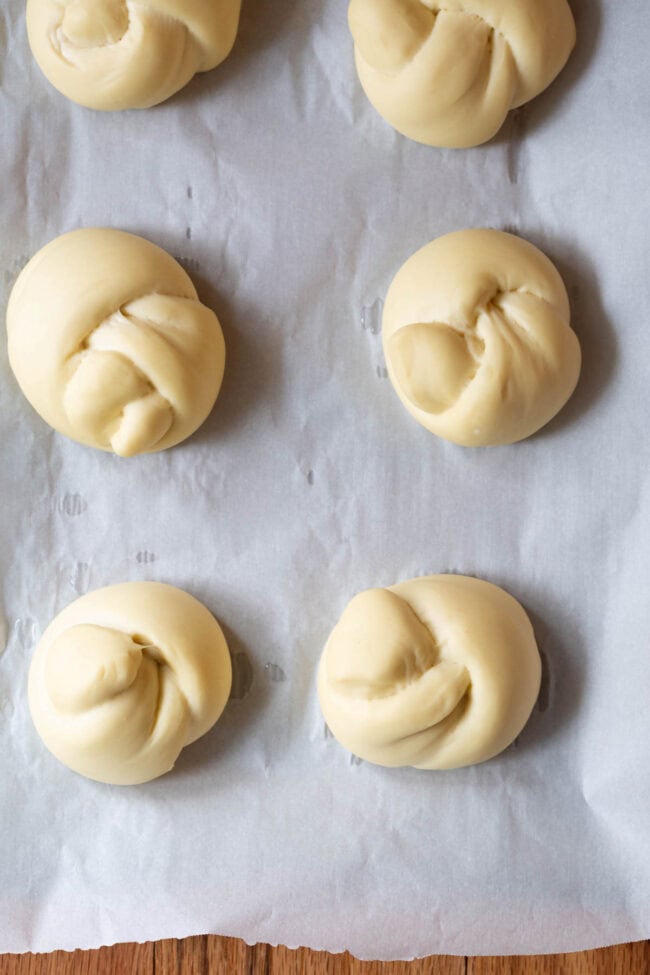 Uncooked garlic knots on a parchment lined baking sheet. 