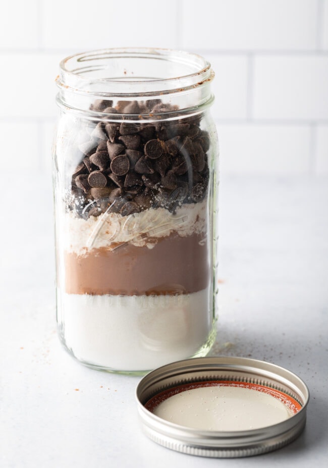 Homemade Ghirardelli brownie mix, dry ingredients layered in a large mason jar with lid off and next to the jar.