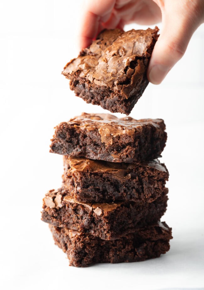 Hand removing a brownie from the top of a stack of 4 remaining brownies.