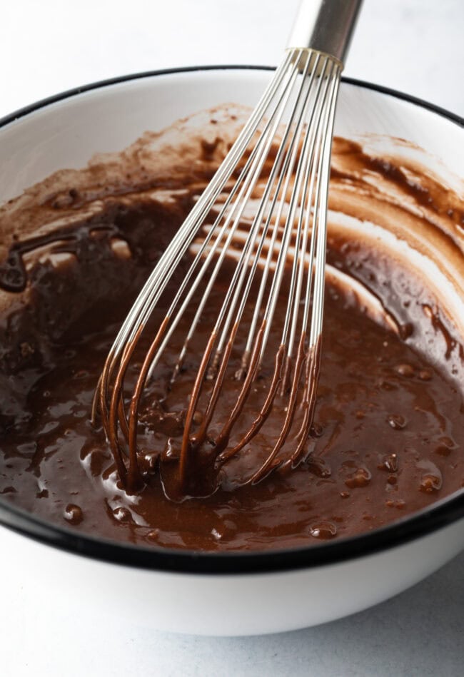 Metal whisk combining wet and dry ingredients into a dark batter.