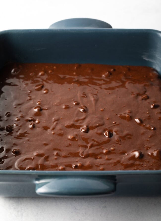 Square baking pan with raw chocolate brownie batter ready to bake.