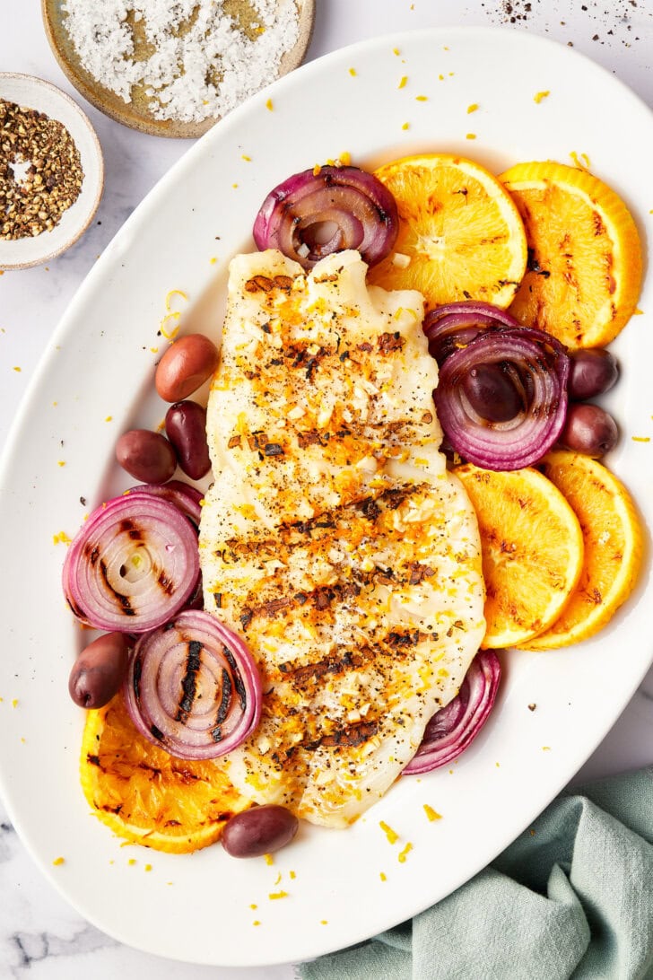 Overhead shot of grilled grouper recipe on a serving platter with grilled citrus, onions and olives. 