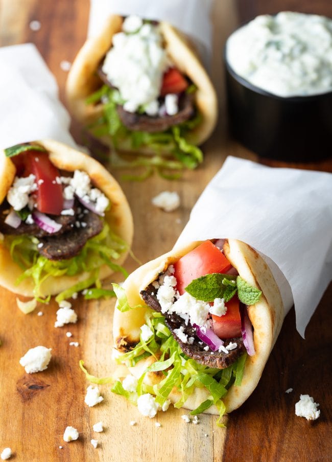 Lamb gyros assembled and wrapped in paper on a wooden surface. 