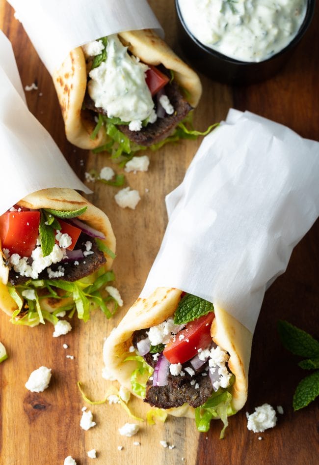 Overhead shot of three assembled lamb gyros wrapped in parchment paper. 