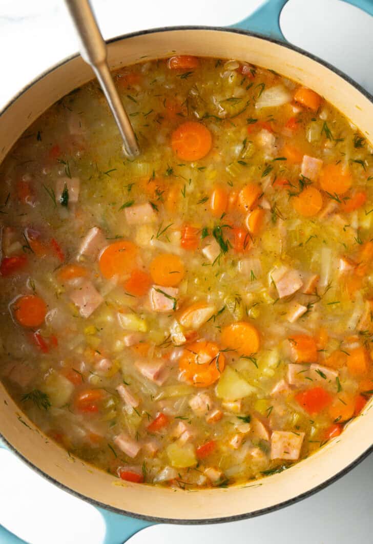 Top down view of chunky veggie cabbage and ham soup in a large blue cooking pot.