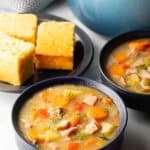 Two black bowls of ham and cabbage soup next to a black plate with 3 squares of cornbread.