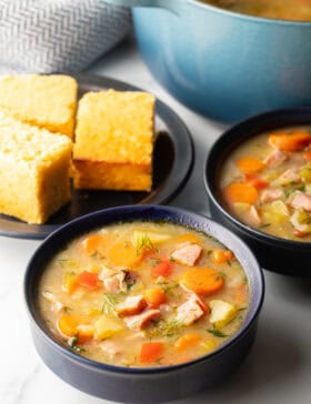 Two black bowls of ham and cabbage soup next to a black plate with 3 squares of cornbread.