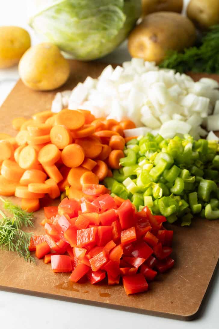 Diced onion, carrots, bell pepper and celery in piles on a brown cutting board.