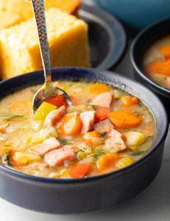 Spoonful of soup held over black bowl of cabbage and ham soup, showing to camera.