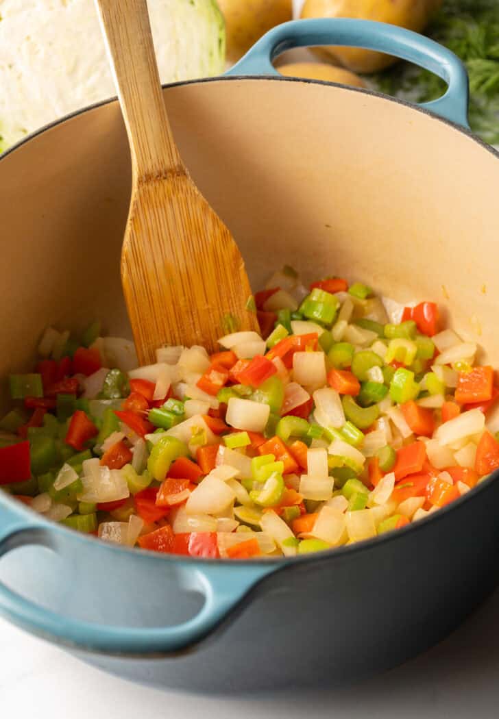 Cooking iced onion, carrots, bell pepper and celery in a large blue cooking pot.