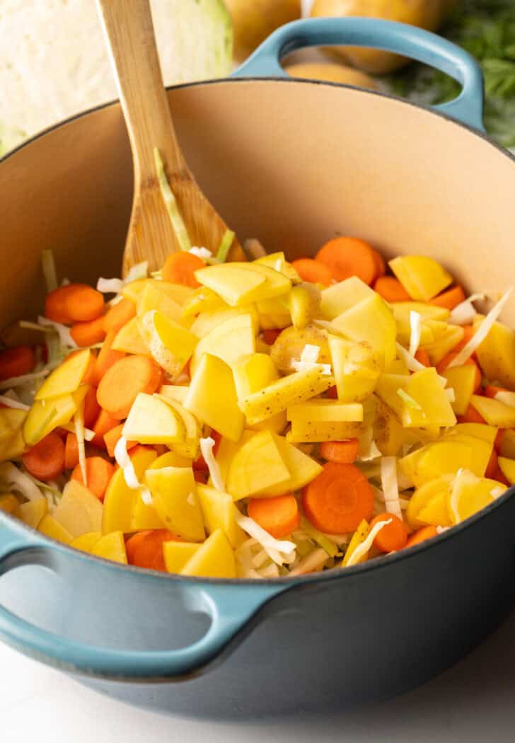 Large blue cooking pot with chunks of potato, carrots, and cabbage.