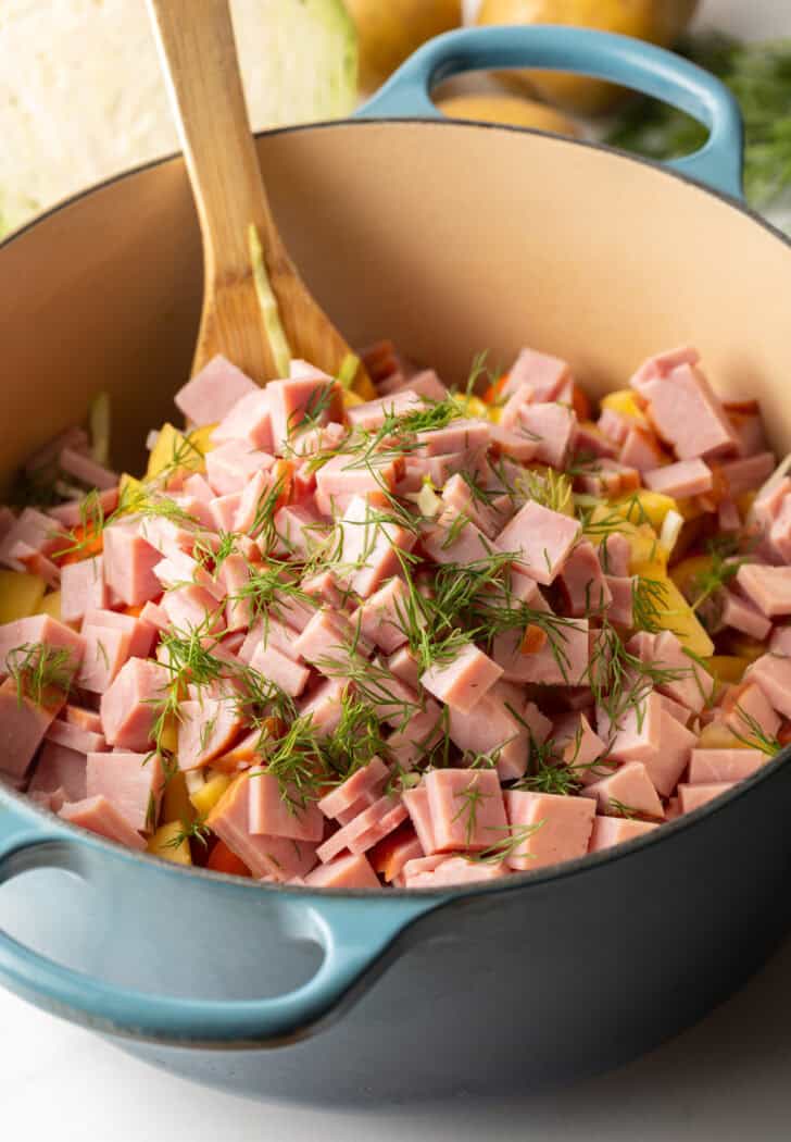 Large blue cooking pot with diced ham, veggies and fresh spices.