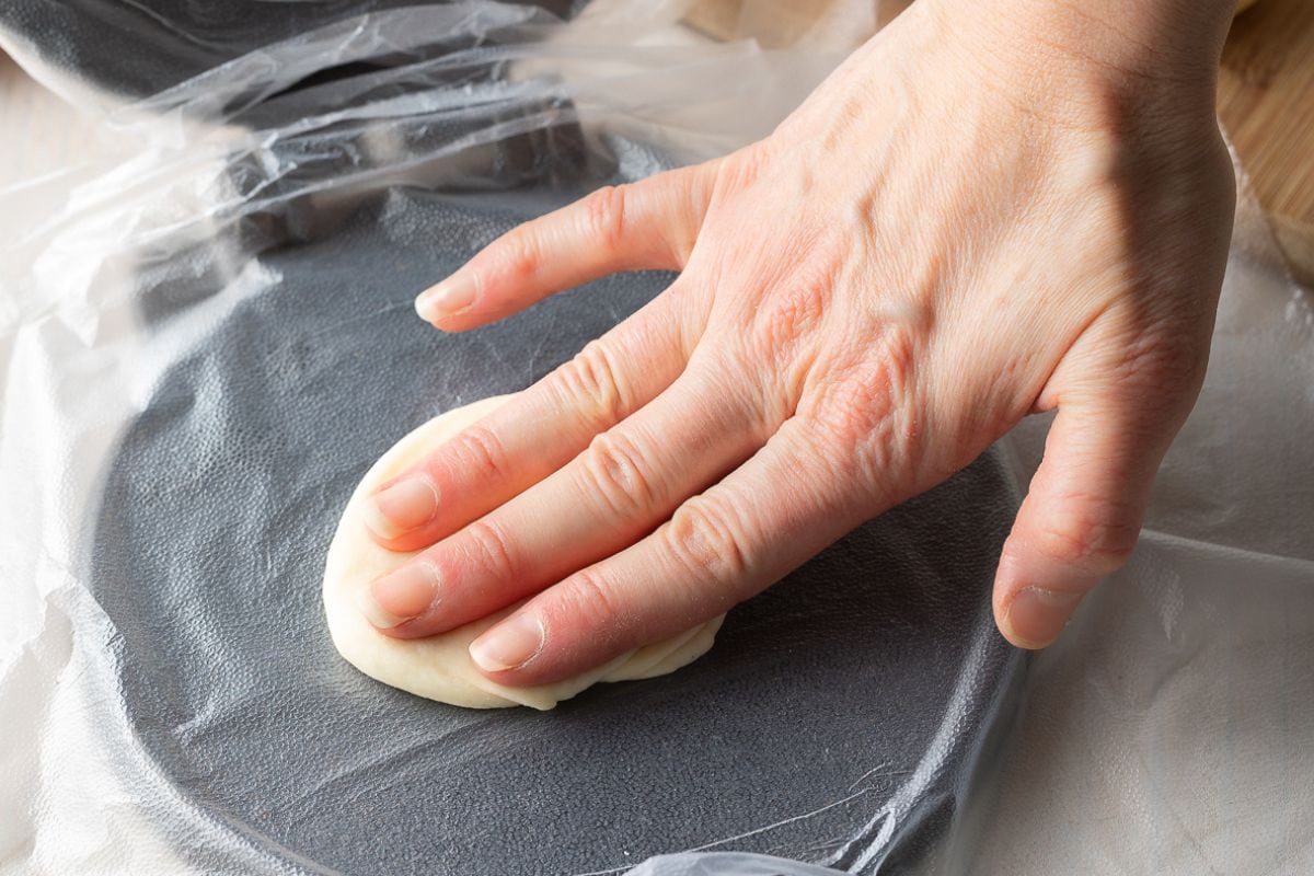 Hand pressing down tortilla dough into a tortilla press. 