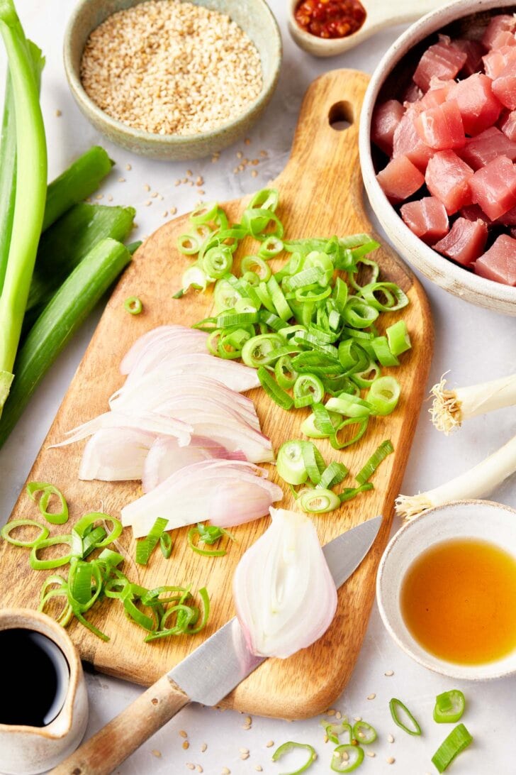 Chopped shallots and green onions on a cutting board with raw tuna in the background. 