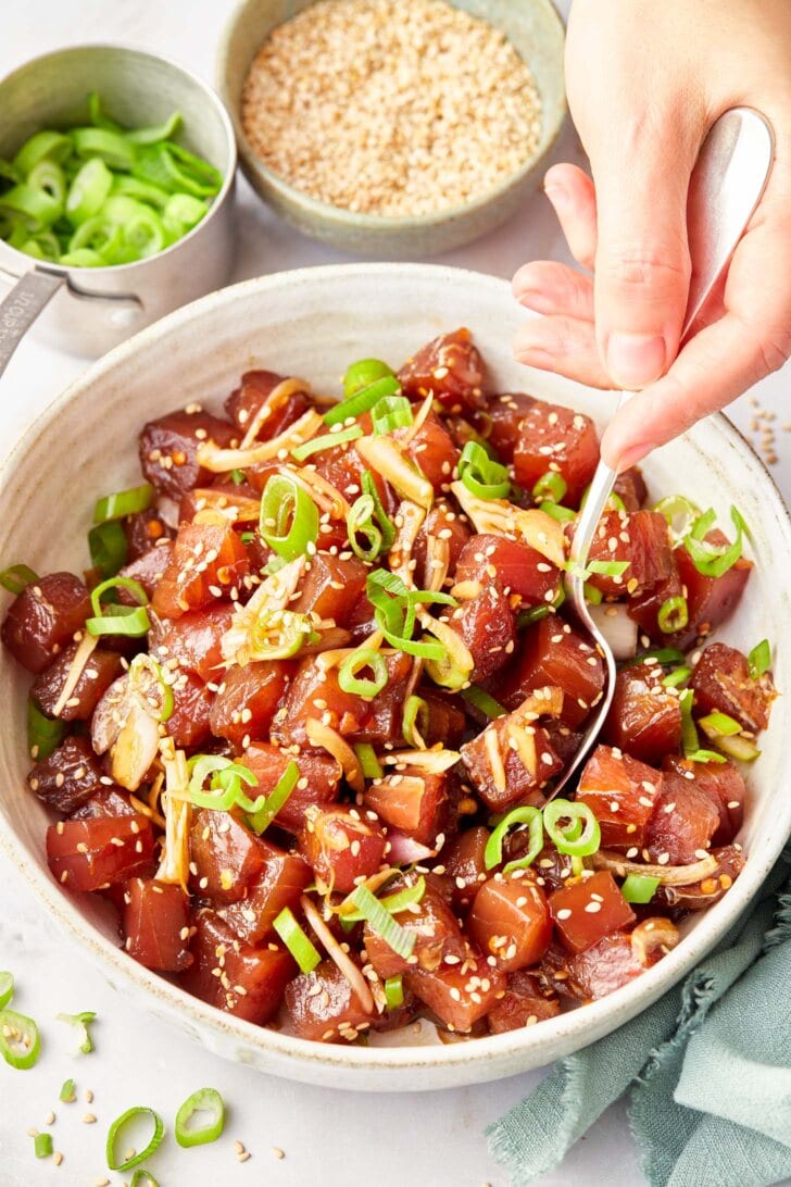 Hand mixing the ingredients for Hawaiian ahi poke in a large bowl. 