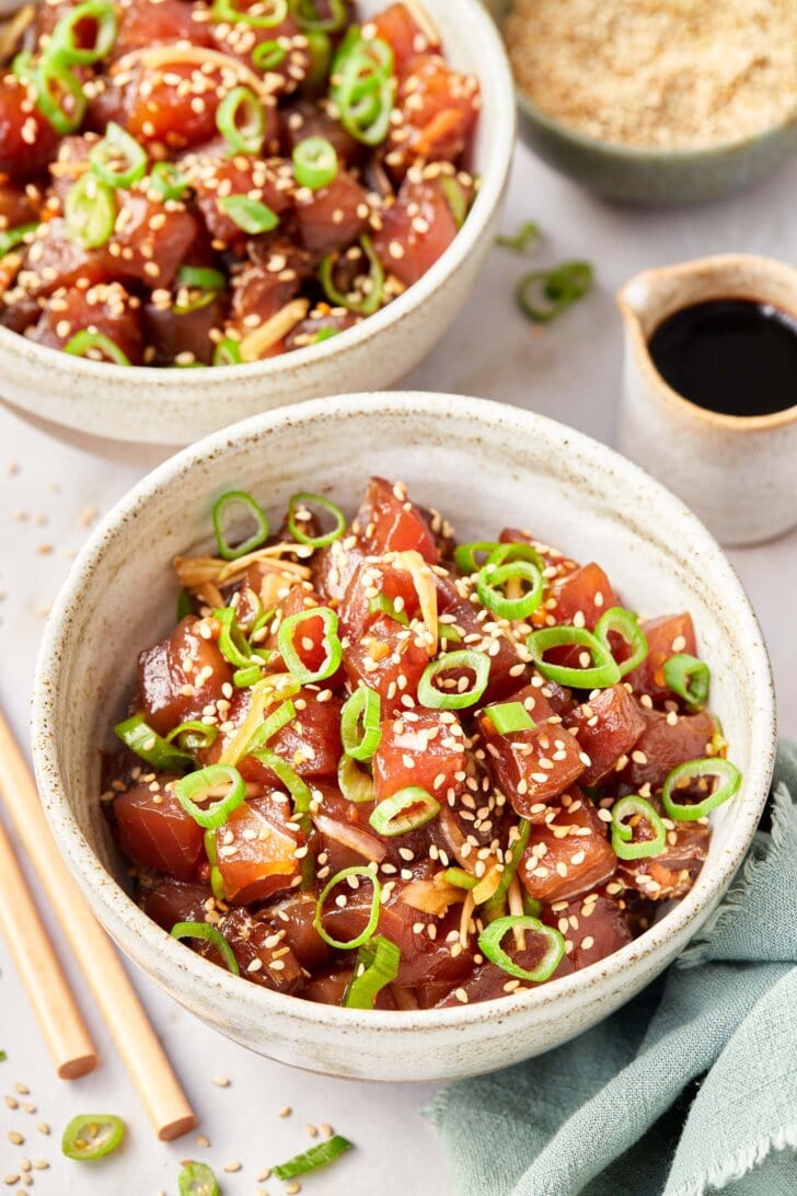 Two bowls full of ahi poke with a side of soy sauce. 