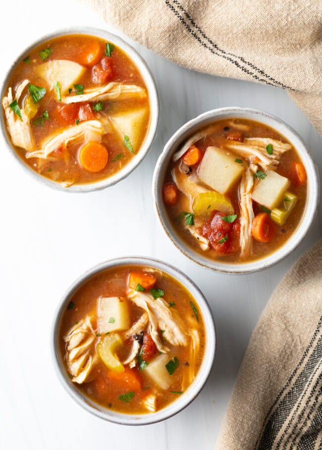 Three bowls of chicken stew slow cooker soup, top down view.