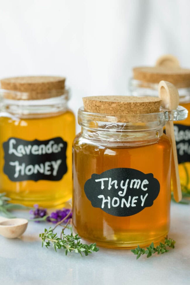 Three small jars of honey labeled "thyme honey", "lavender honey", and "rosemary honey". 