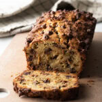 Loaf of high protein banana bread with chocolate chips. 1 slice is cut in front of the loaf.