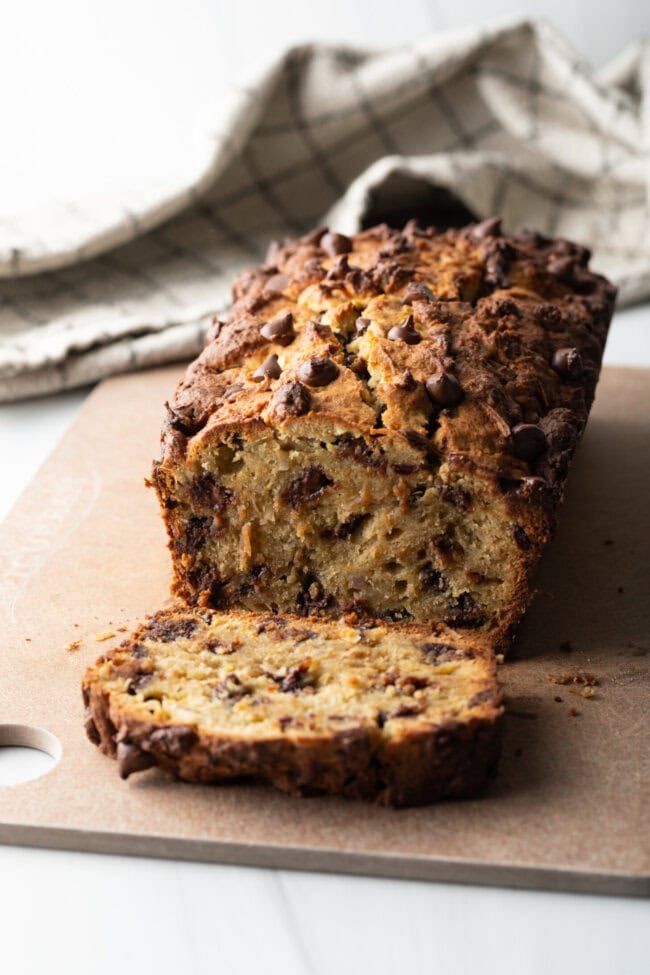 Loaf of high protein banana bread with chocolate chips. 1 slice is cut in front of the loaf.