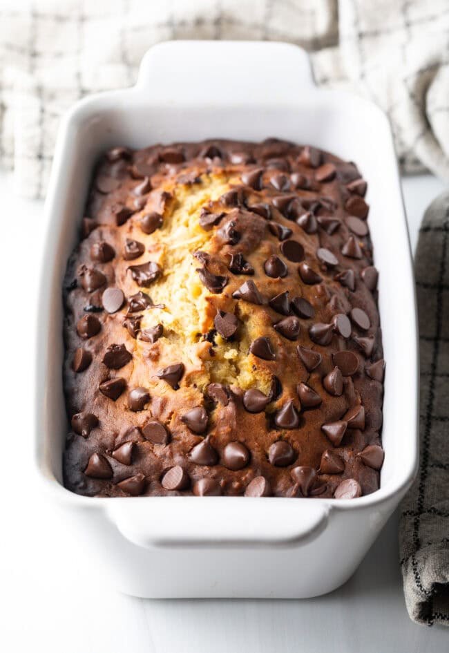 Baked loaf of low carb high protein banana bread with chocolate chips in a white loaf pan.