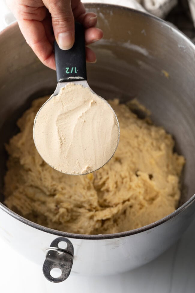 Hand with measuring cup adding sweetener to the batter.