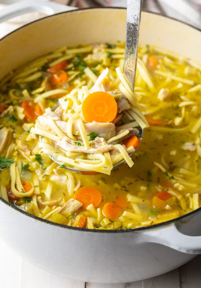 Ladle full of best chicken noodle soup above the pot of the rest of soup. 