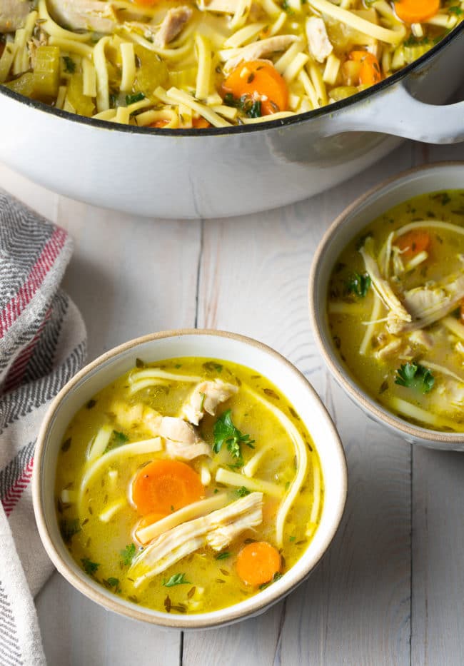 A couple servings of soup in a few bowls next to the large pot of soup. 