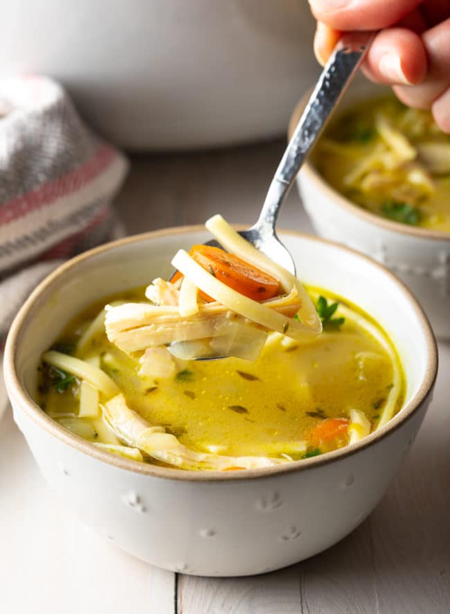 Showing off a spoonful of homemade chicken soup with the bowl of soup underneath it. 