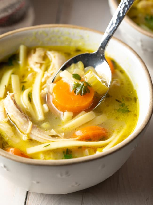 Bowl of spicy chicken noodle soup with a spoon scooping up a bite. 