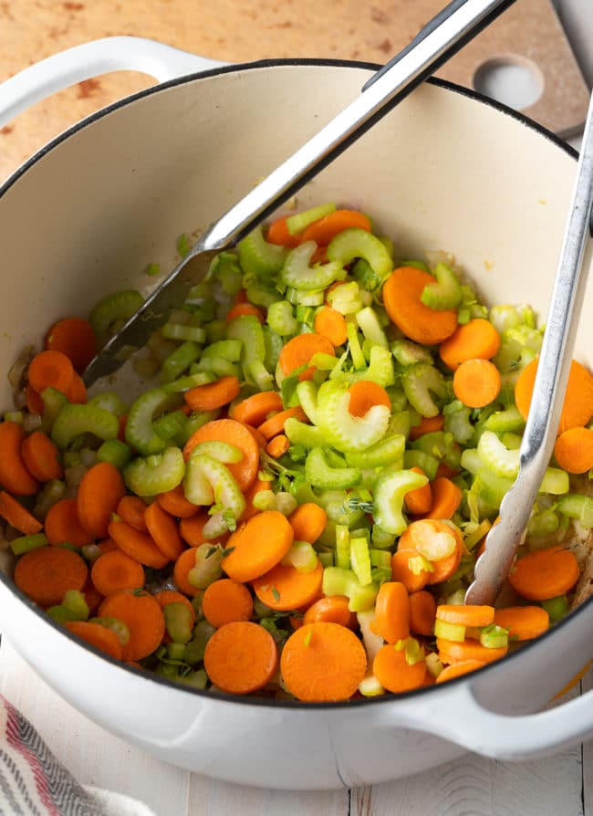 Carrots and celery being sautéed in a large pot. 