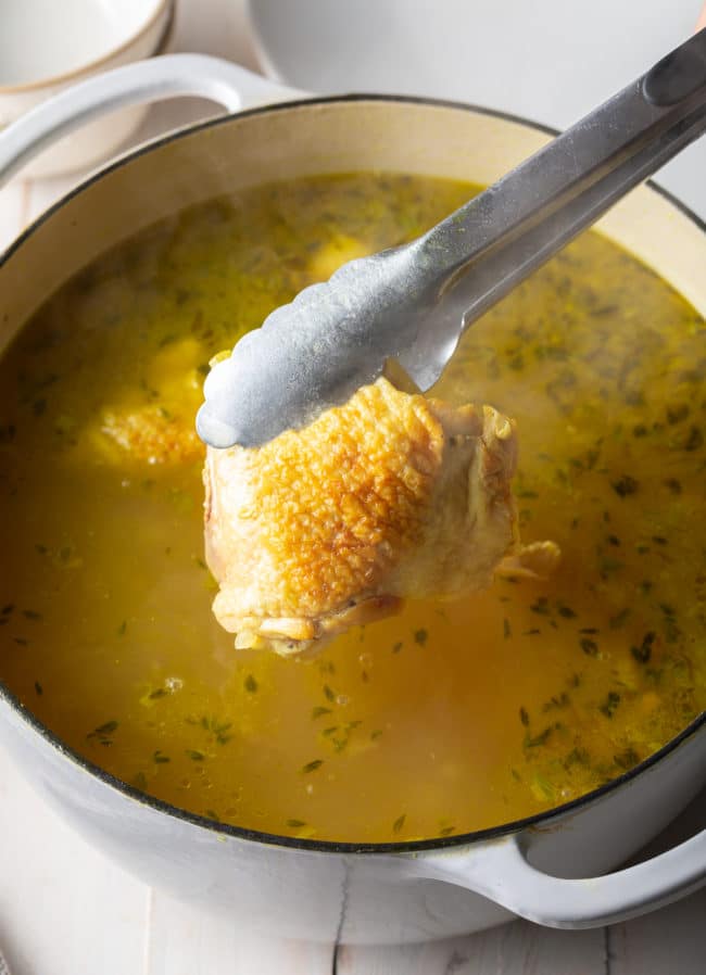 Chicken thighs being placed into a pot of soup. 