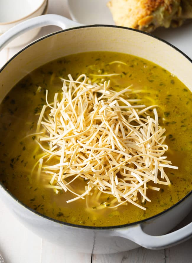 Dried noodles being placed in a pot of soup. 